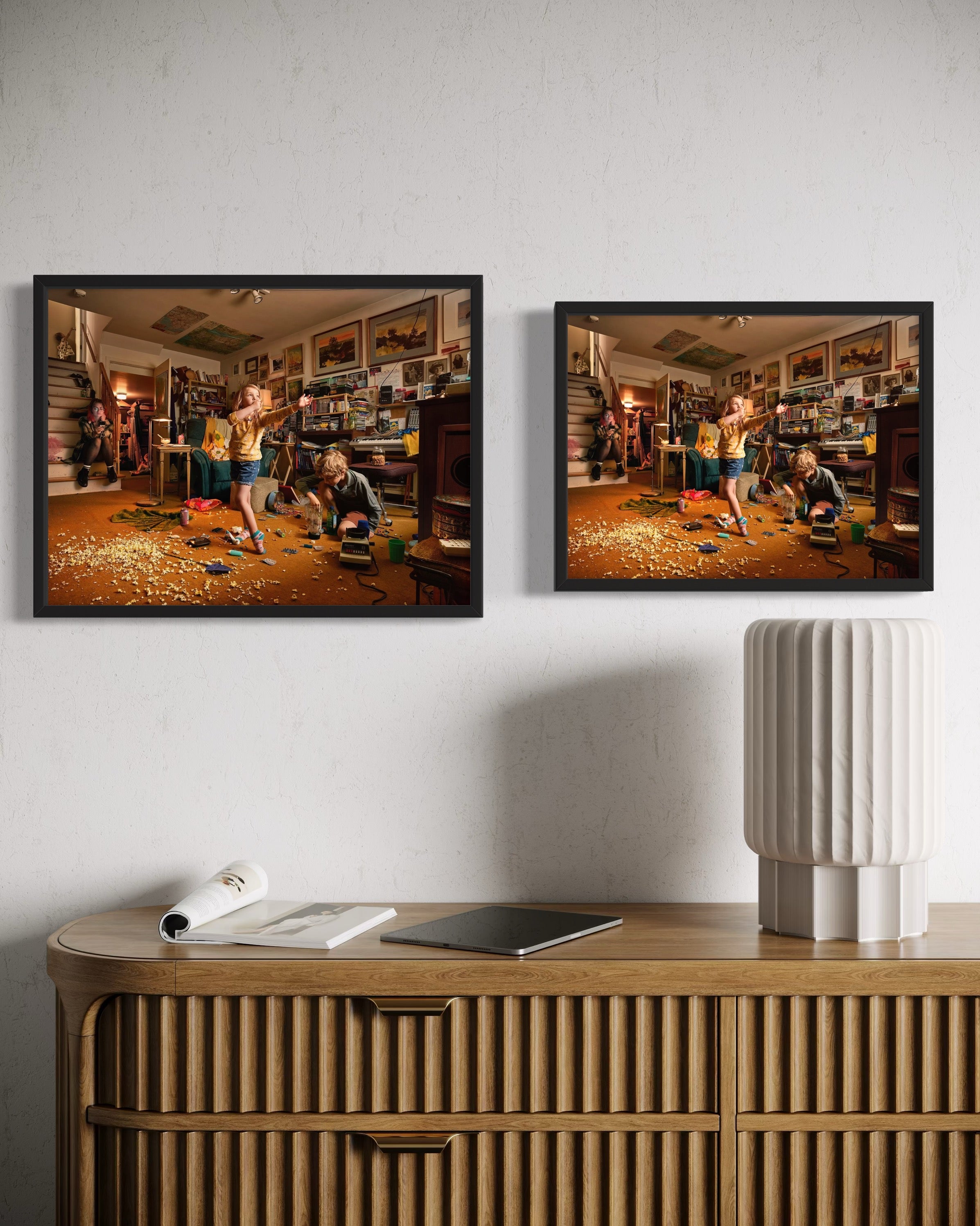 Two framed photographs of children playing in a room on a white wall above a wooden console table.
