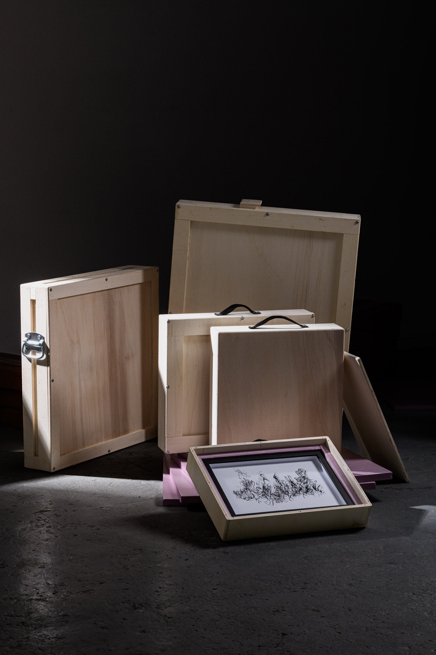 A framed artwork nestled in foam padding inside a wooden art crate, surrounded by other handcrafted crates with black fabric handles, illustrating secure and elegant artwork packaging.