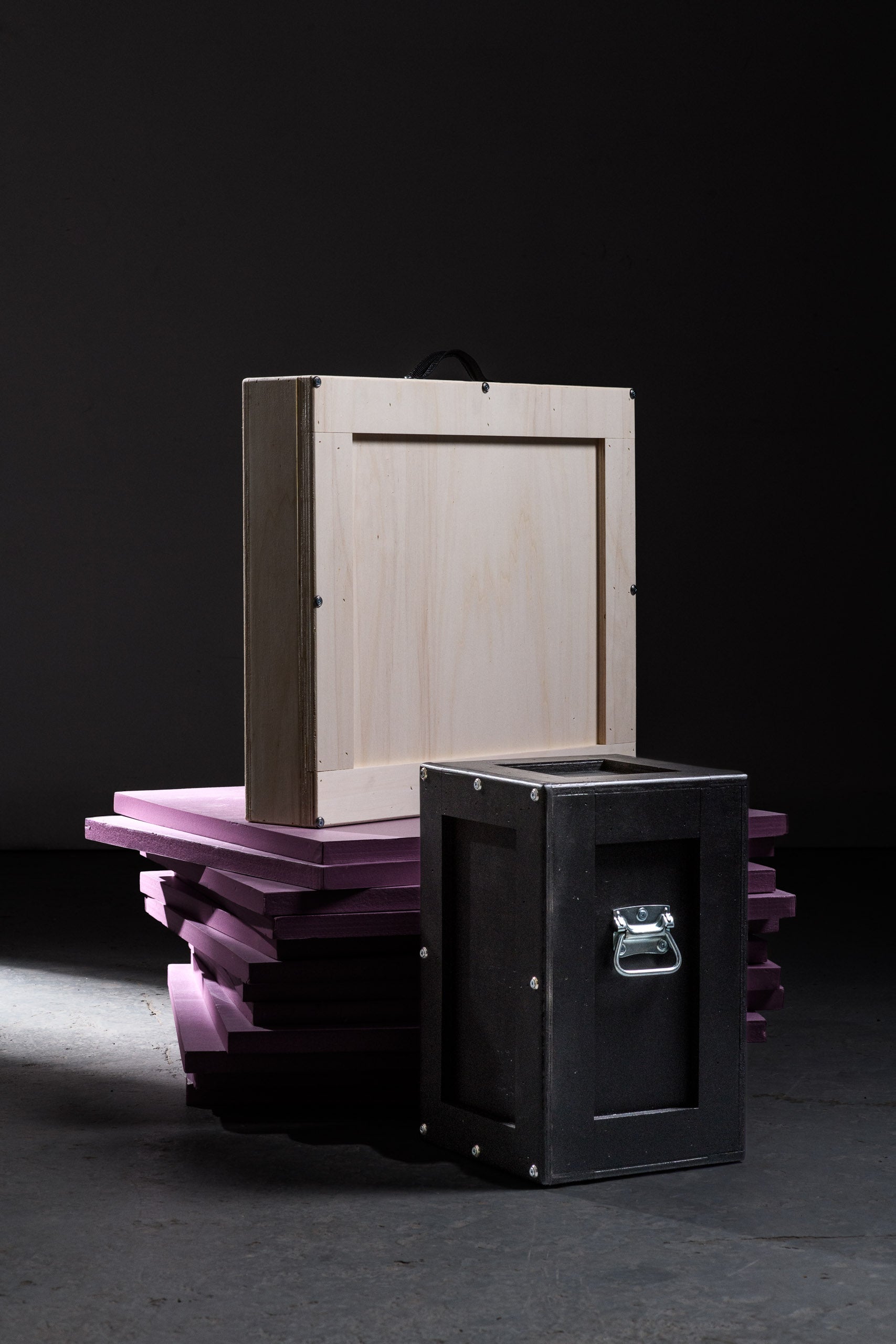  A wooden art crate standing on stacked purple foam sheets beside a sleek black crate, showcasing the layered protection and elevated presentation of valuable pieces.