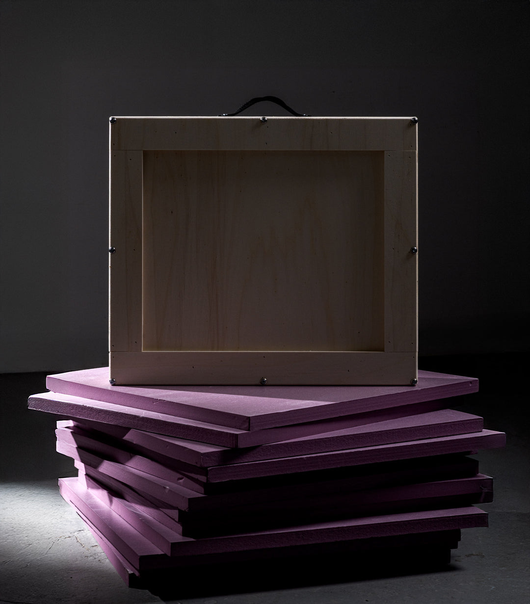 A single light-toned wooden crate displayed on stacked purple insulation foam, against a dark backdrop to highlight the quiet luxury of professional art crating.