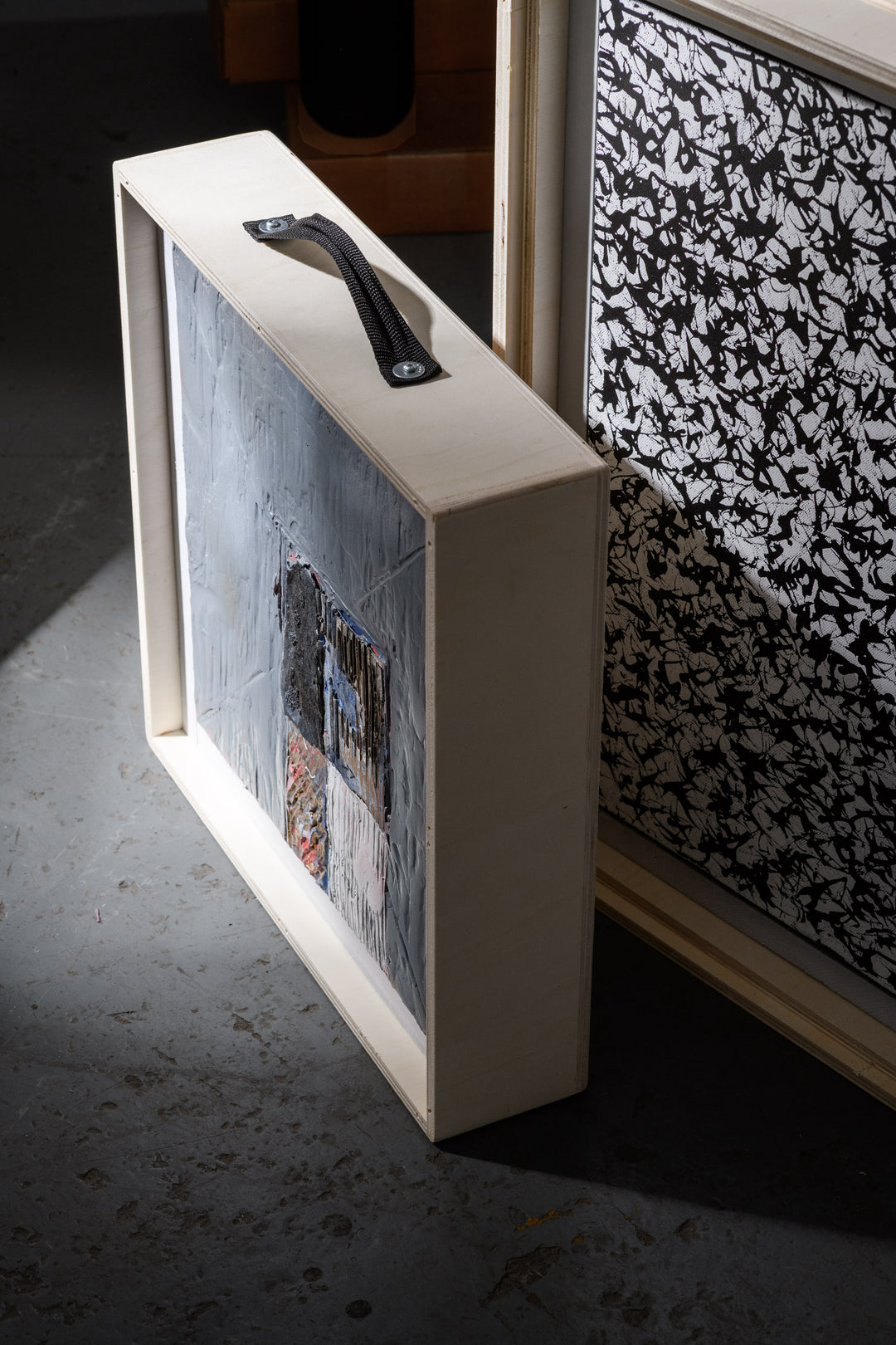 Detail view of a wooden crate carrying a heavily textured painting, with another black-and-white patterned artwork beside it, reflecting the care given to each individual piece.