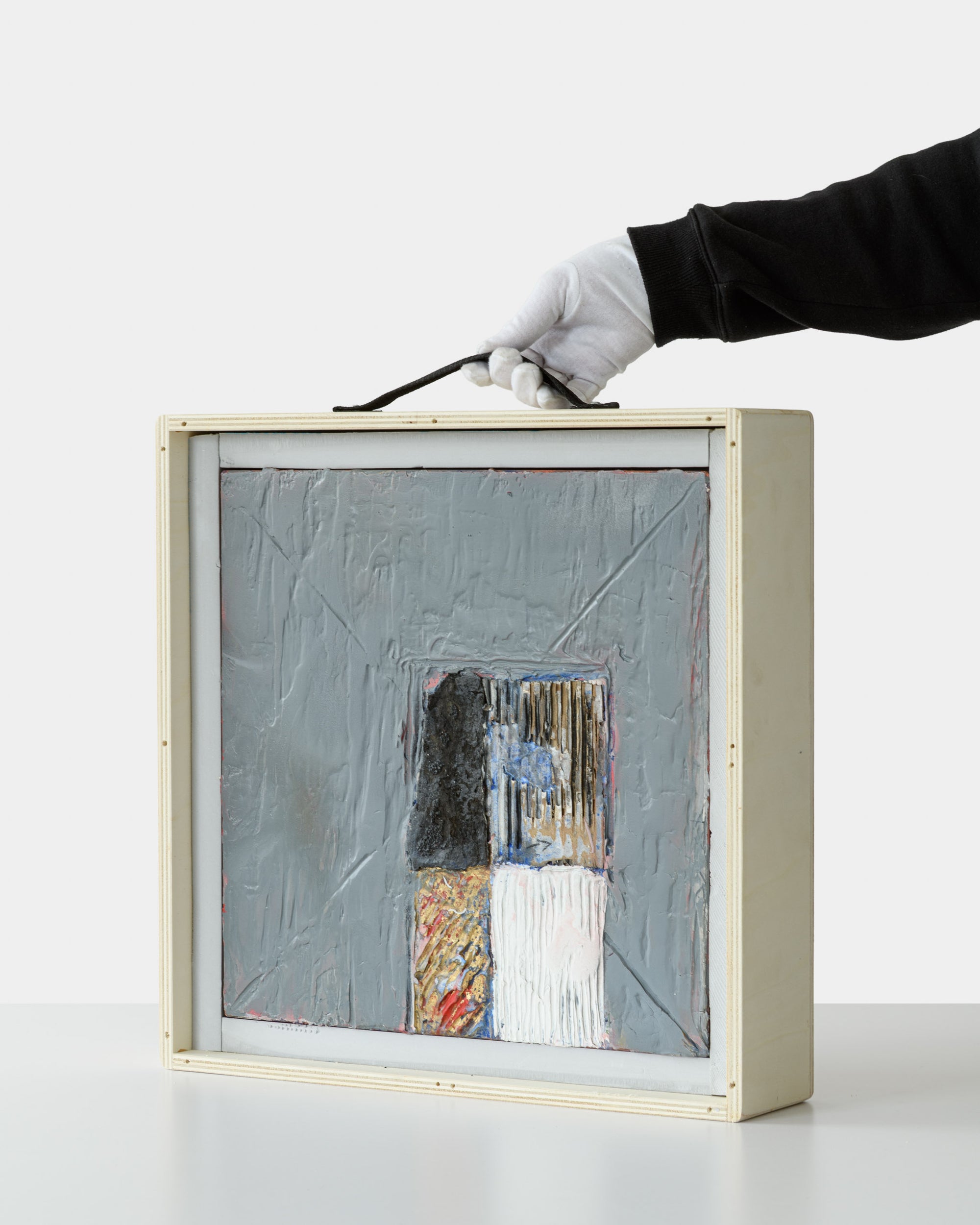 Original textured painting by Jean Michel Correia packed inside a custom wooden crate, held by a gloved hand via a black fabric handle.