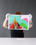 Artist holds up a limited edition print for inspection, wearing white gloves against a neutral grey background.