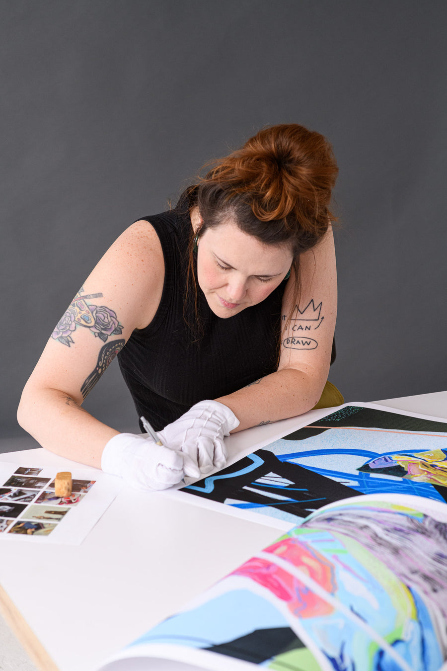Artist signs a vibrant abstract print while referencing a contact sheet for visual consistency, demonstrating attention to detail.