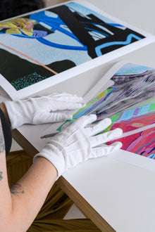  White-gloved hands gently position a limited edition print during the signing process, ensuring precise handling and placement.
