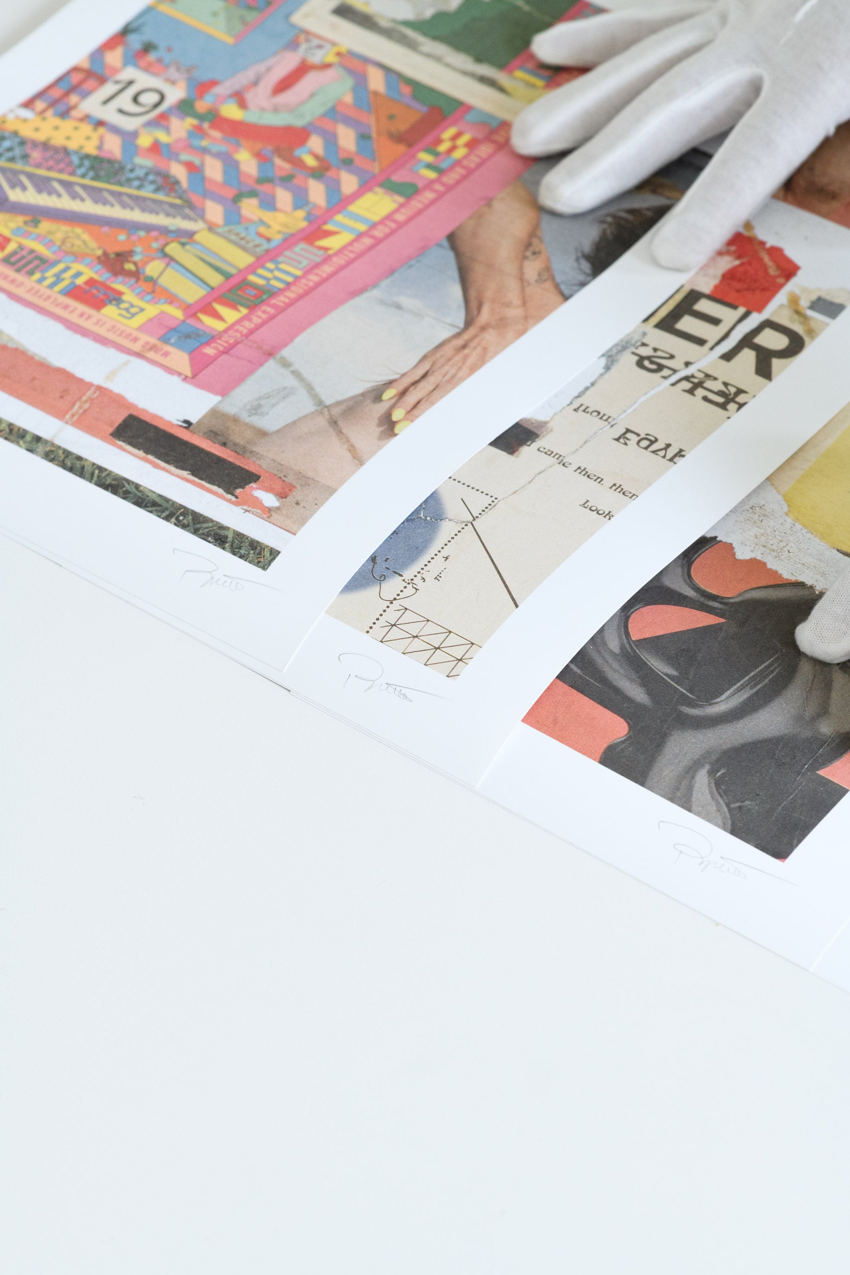 Close-up of three limited edition collage prints with visible artist signatures at the bottom, handled carefully with white gloves.