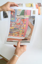 A person holds up a vibrant art print featuring colorful, surreal collage imagery, showing the edition number and artist signature.