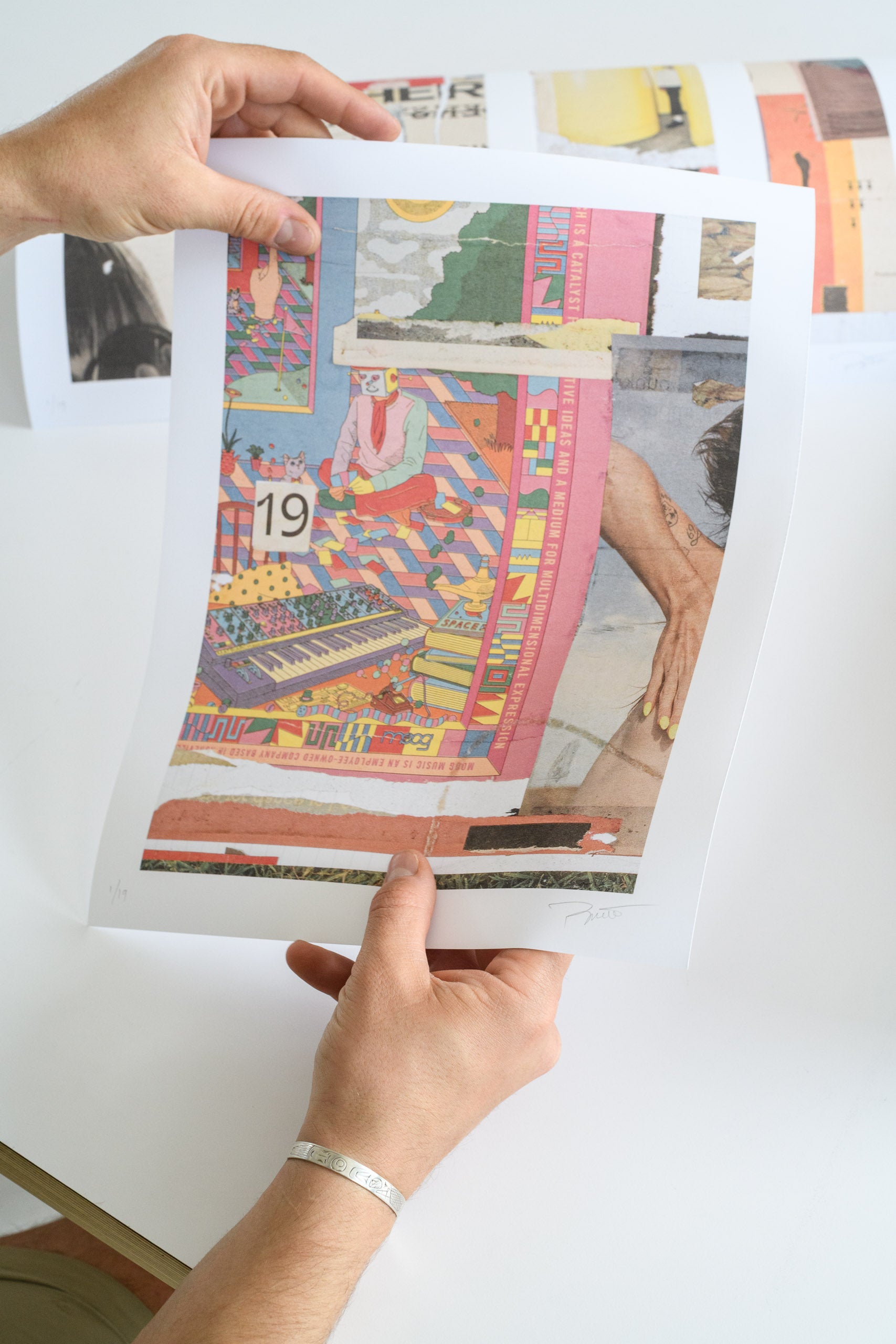A person holds up a vibrant art print featuring colorful, surreal collage imagery, showing the edition number and artist signature.
