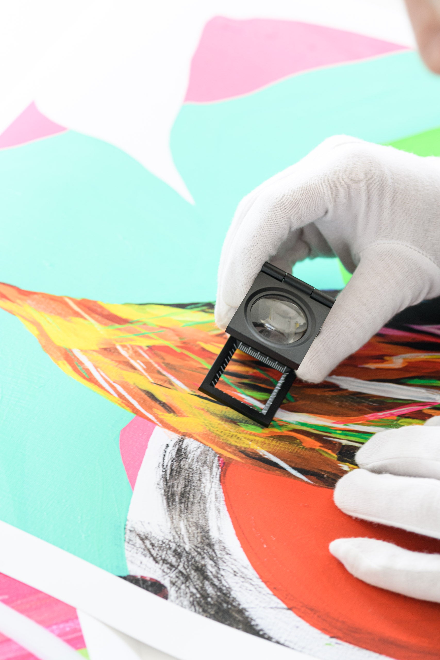 Hand wearing a white glove holding a small black tool over a colorful abstract painting.