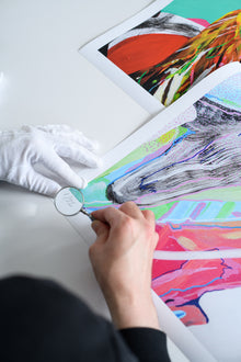 A limited edition print marked “1/22” is being carefully inspected under magnification by a person wearing white gloves, showcasing professional art quality control.