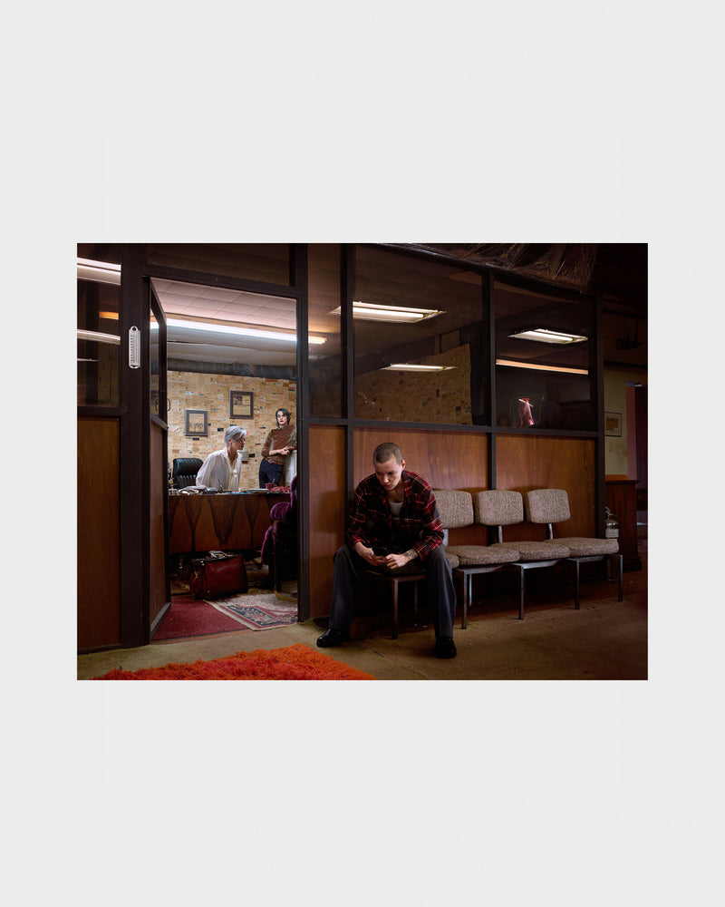 Photograph of a Person sitting in a waiting room with others in the background