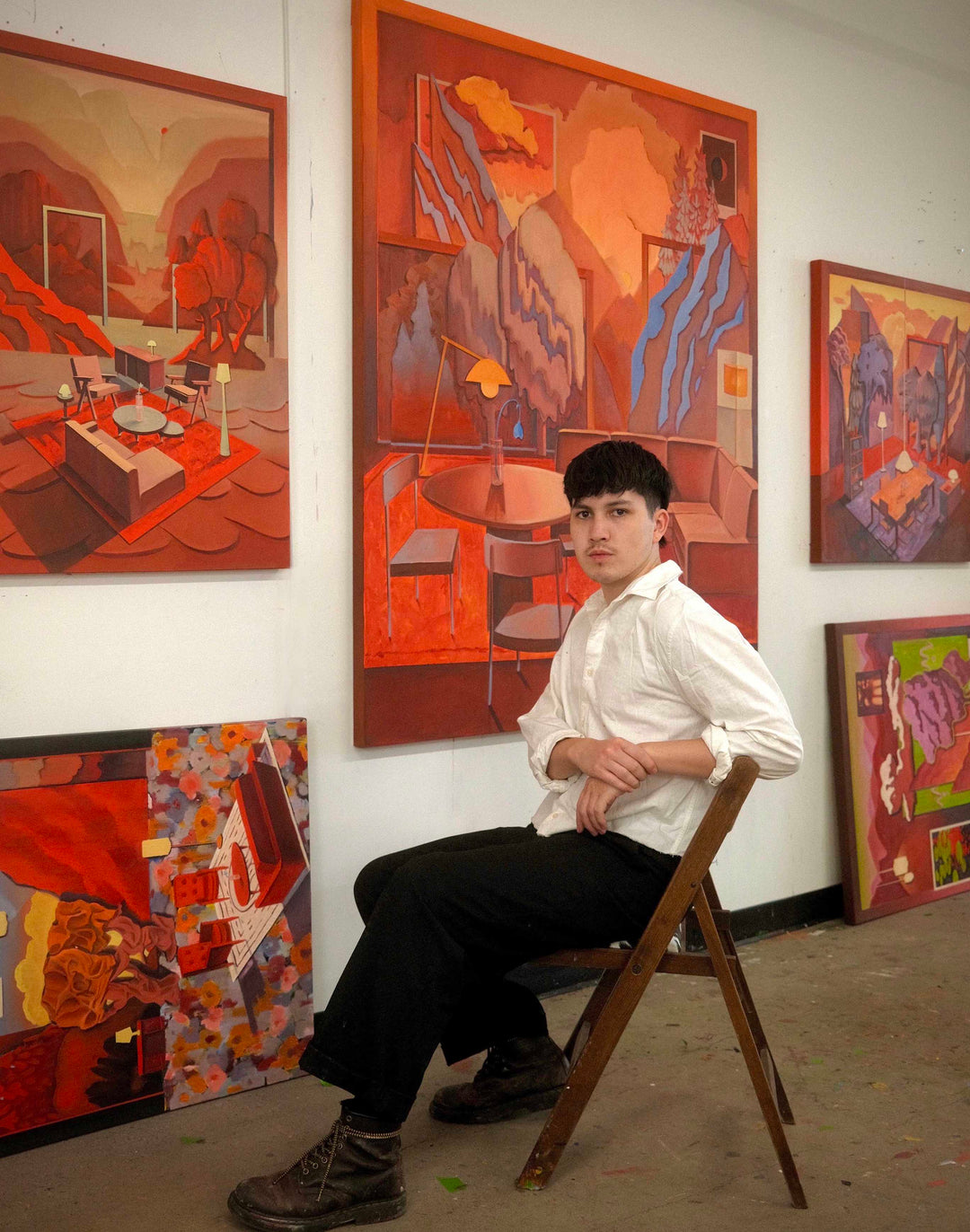 Man sitting on a chair in front of colorful abstract paintings in an art gallery.