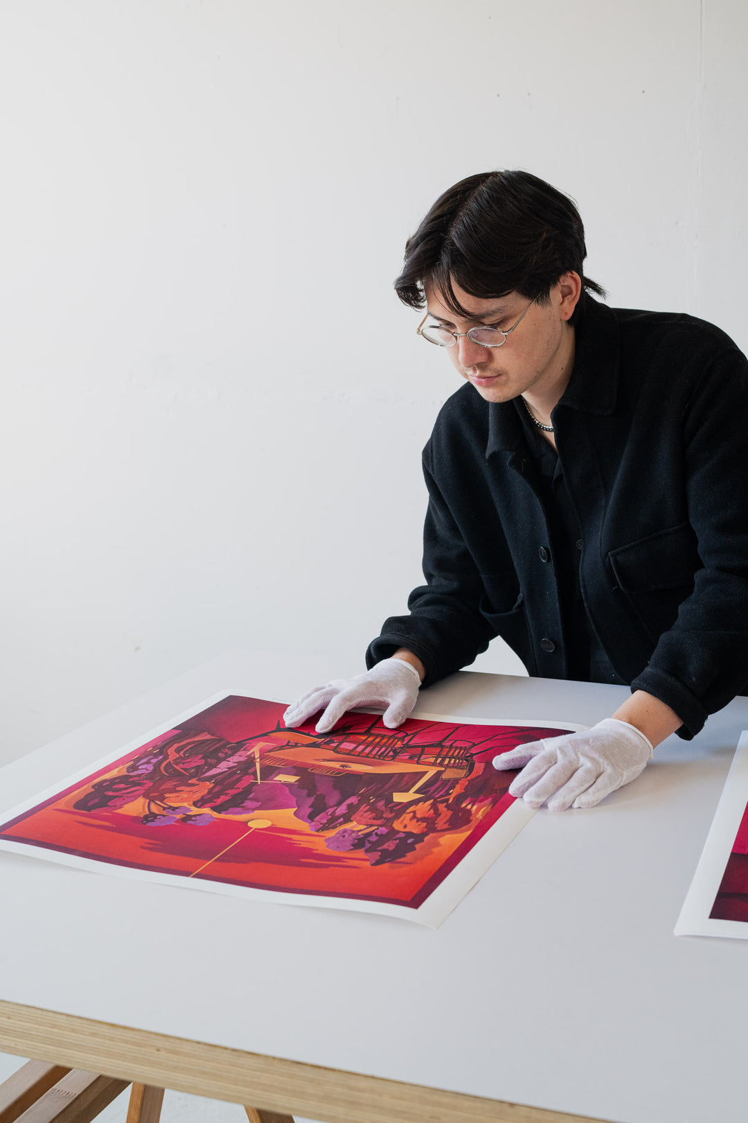 Artist wearing gloves and looking at a colorful print on a table.