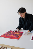 Artist wearing gloves and looking at a colorful print on a table.
