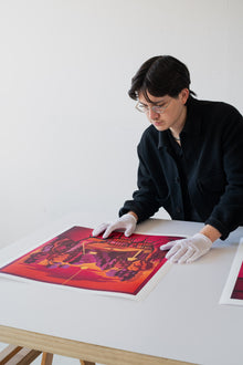 Artist wearing gloves and looking at a colorful print on a table.