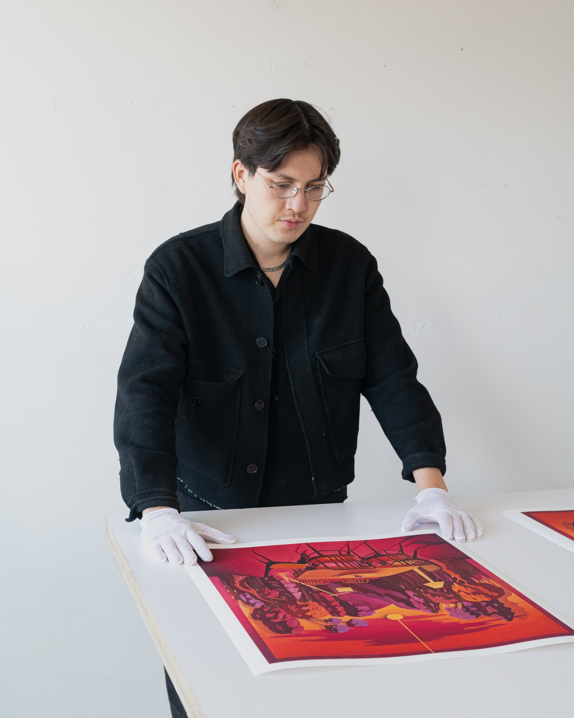 Artist wearing gloves and looking at a colorful print on a table.