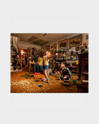 Photograph of Two children playing in a cluttered room with toys and furniture.