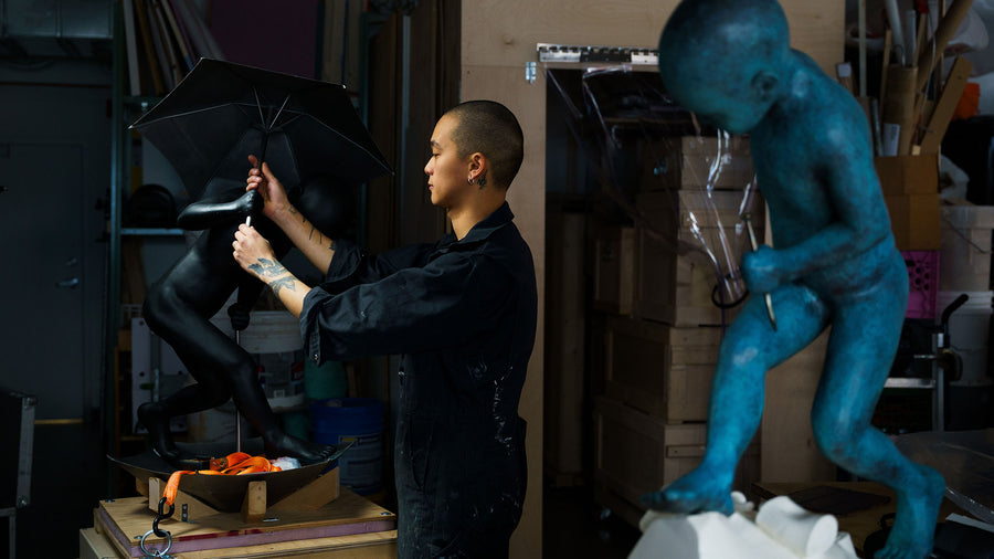 Person working on a sculpture in a studio with a blue figure and black umbrella.
