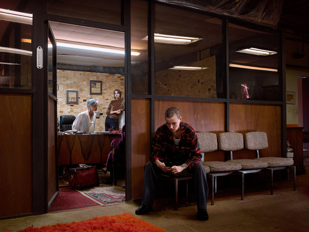 Photo of a Person sitting on a bench in a waiting room with others in the background