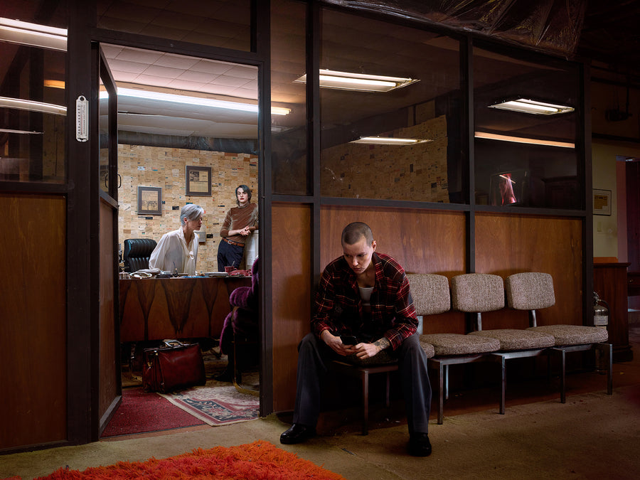 Photo of a Person sitting on a bench in a waiting room with others in the background